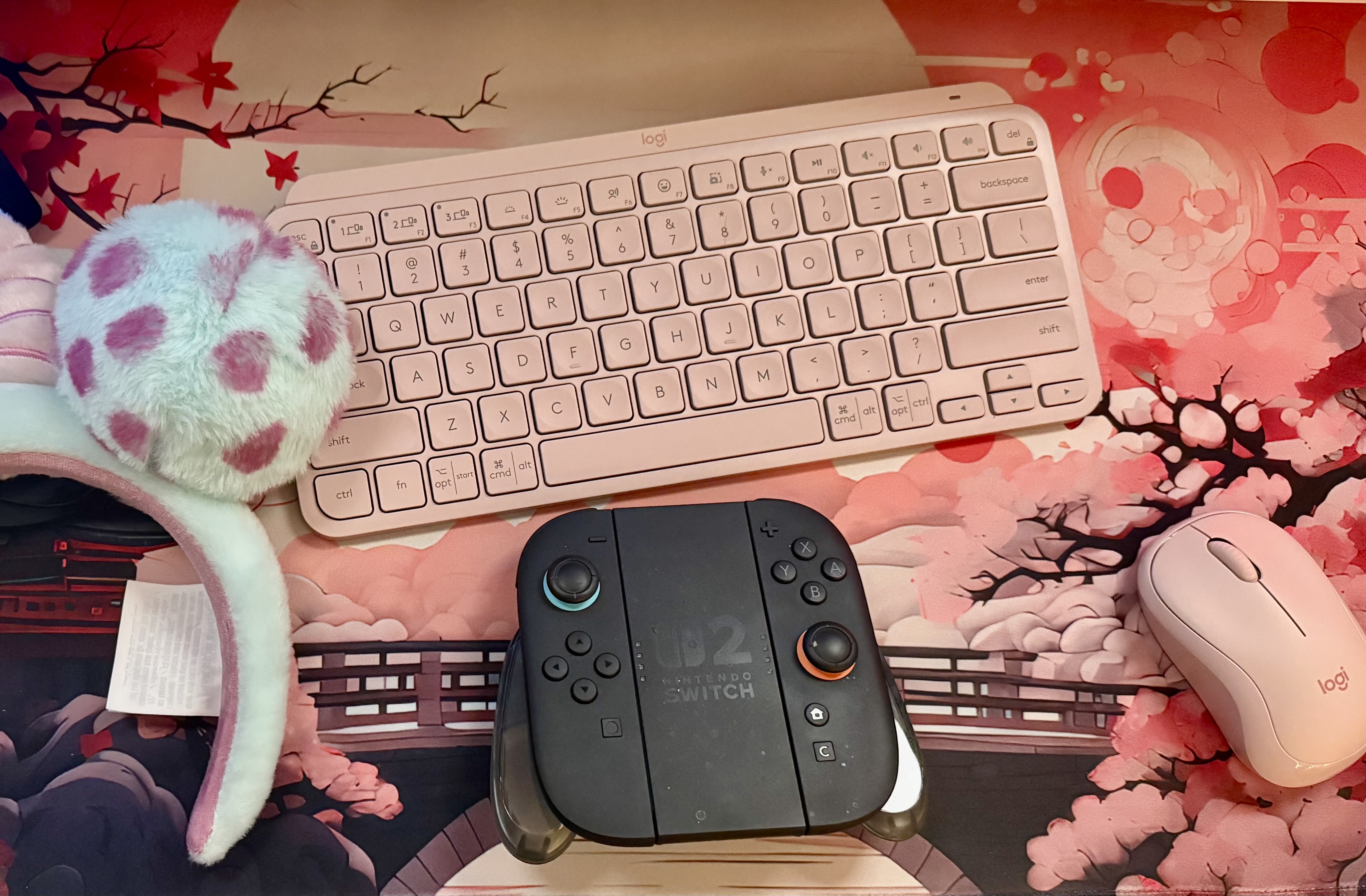 Pink gaming setup with Logitech keyboard, Nintendo Switch, and cherry blossom desk mat