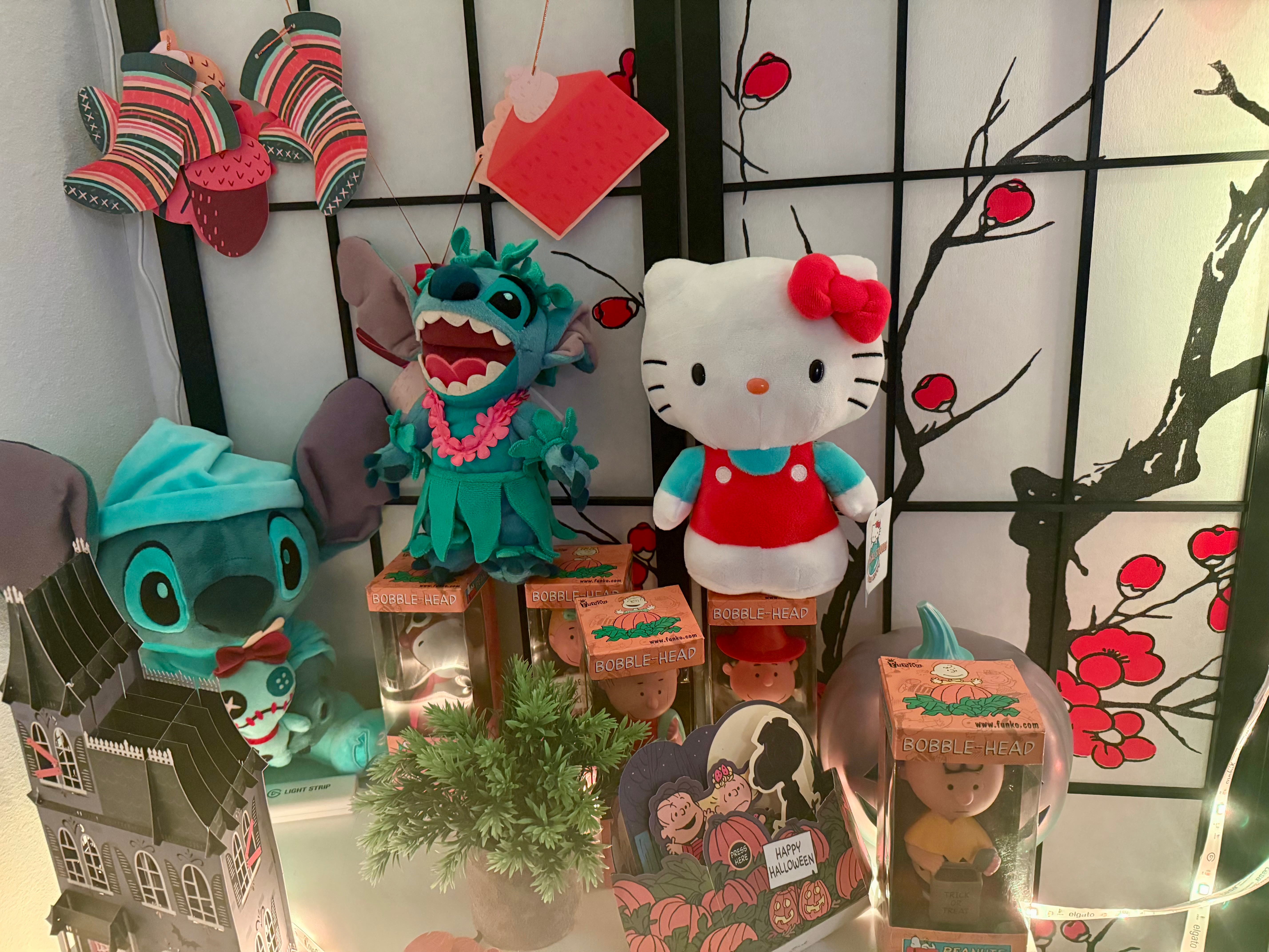 Collection of plushies including Stitch, Hello Kitty, and Charlie Brown bobbleheads with Halloween decorations